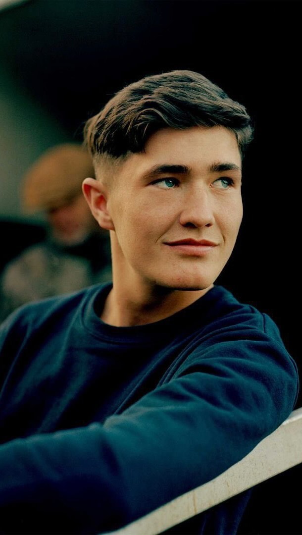 Portrait of a young adult male looking off to the side, wearing a navy sweater in an indoor setting, with soft natural light.