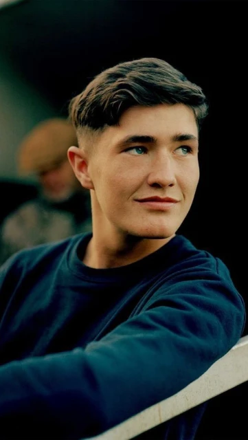 Portrait of a young adult male looking off to the side, wearing a navy sweater in an indoor setting, with soft natural light.