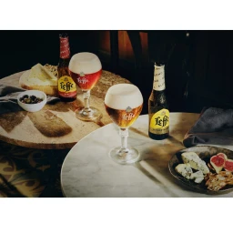 Leffe beer bottles and glasses with thick foam head on round marble and wooden tables with cheese, olives, and figs.