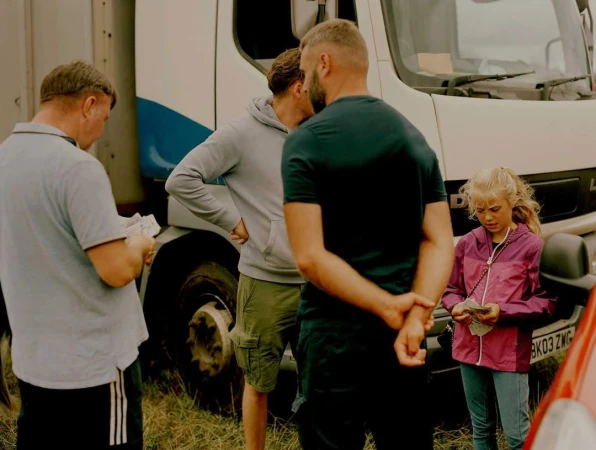Group of four people standing outdoors near a large white and blue truck holding paper currency