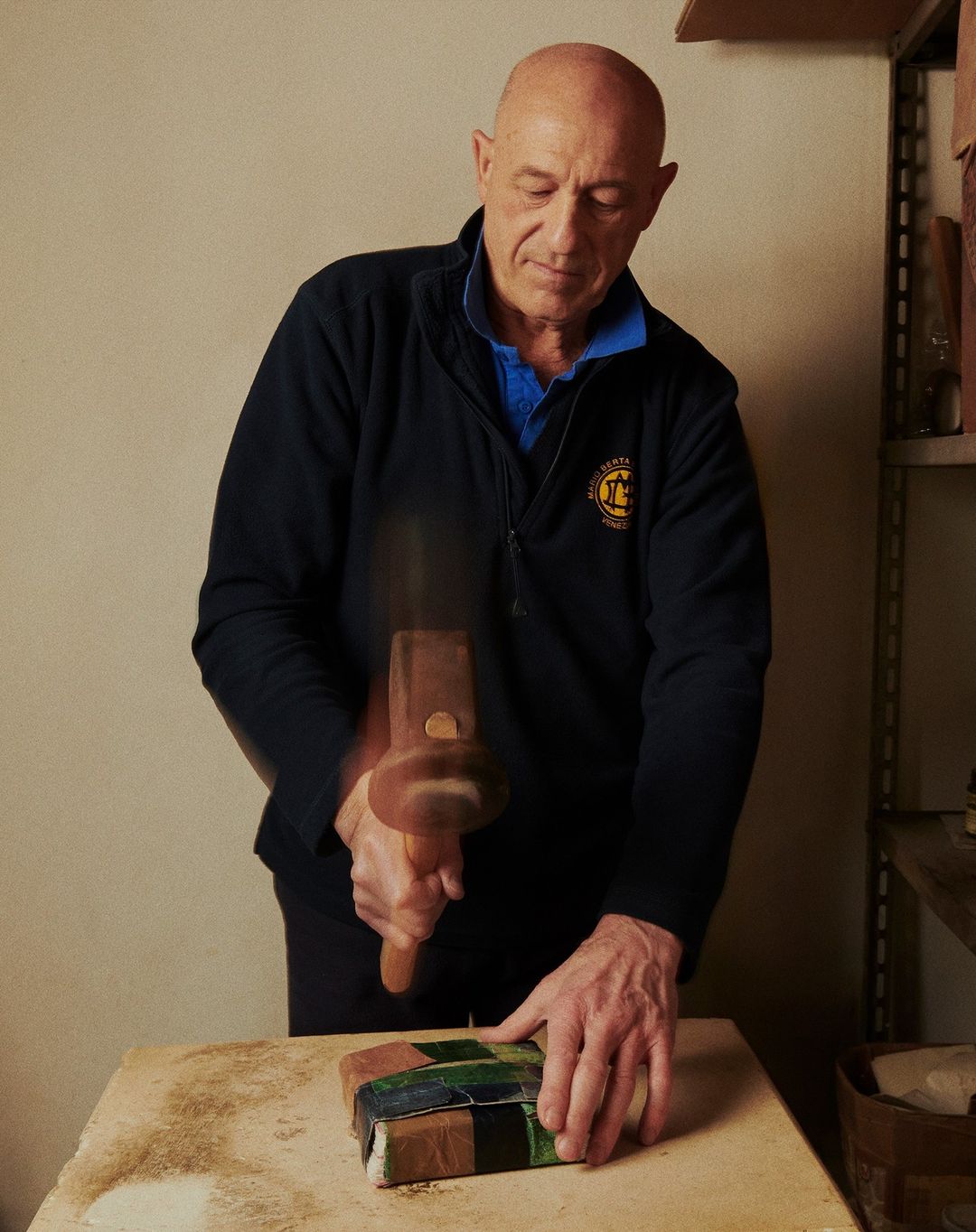 Craftsman hammering mosaic tiles, creating art in a studio. Adult male artist focused on craft, interior setting, clear view of process.