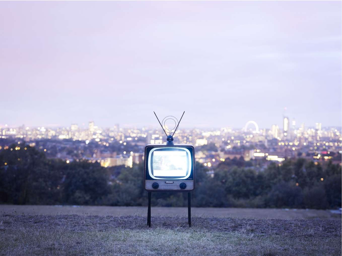 Vintage television set displayed outdoors against a twilight cityscape backdrop, blending technology and urban scenery.