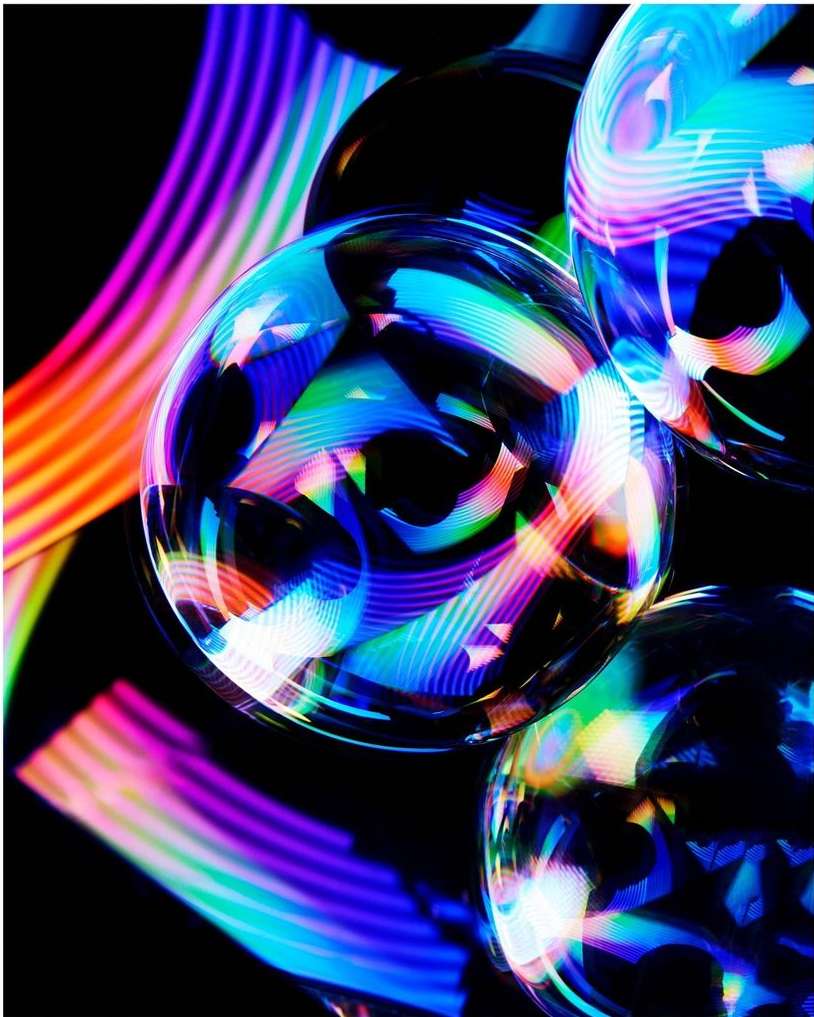 Abstract macro image of soap bubbles with colorful light streaks on a black background, creating a vibrant and surreal visual.