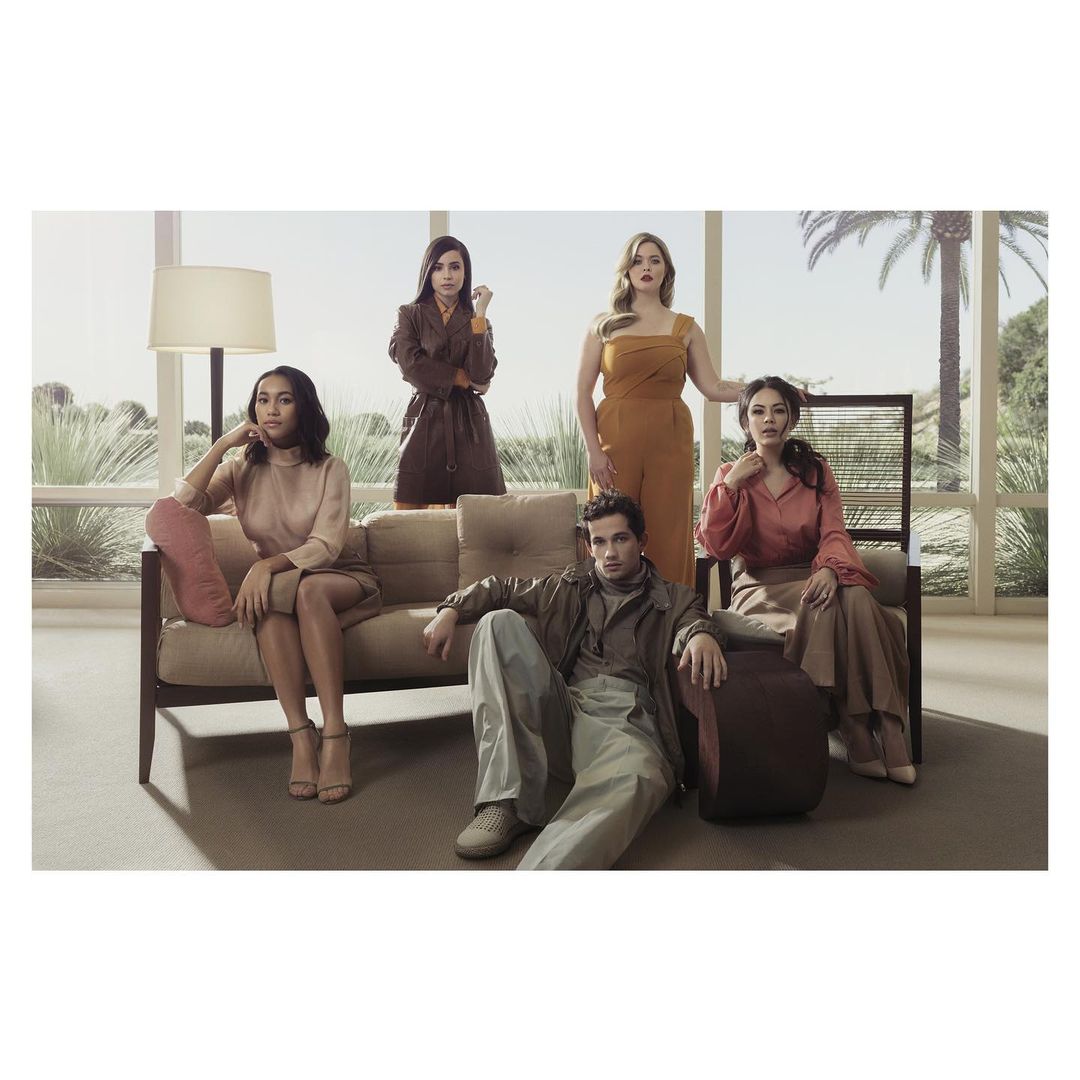 Group of five people poses on and around a modern beige sofa in a sunlit indoor setting, with palm trees visible through a large window.