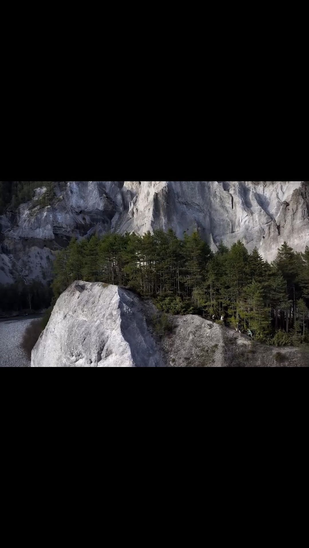 Scenic view of a rock formation with trees on top, with a rugged cliff face and a river visible in the background on a bright day.