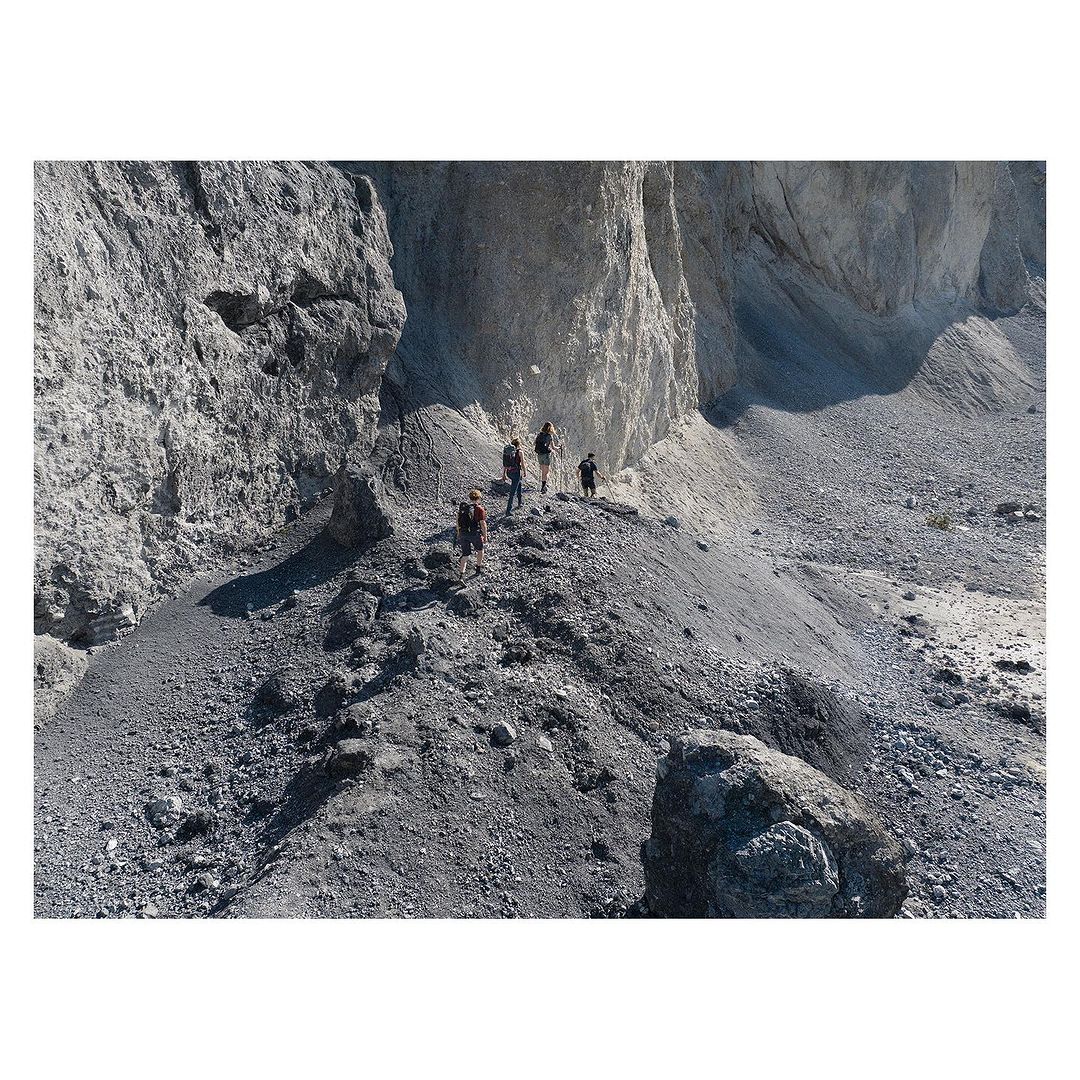 A group of hikers on a rocky mountain path. The path is narrow, and the hikers are surrounded by tall rock formations.