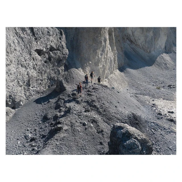 A group of hikers on a rocky mountain path. The path is narrow, and the hikers are surrounded by tall rock formations.