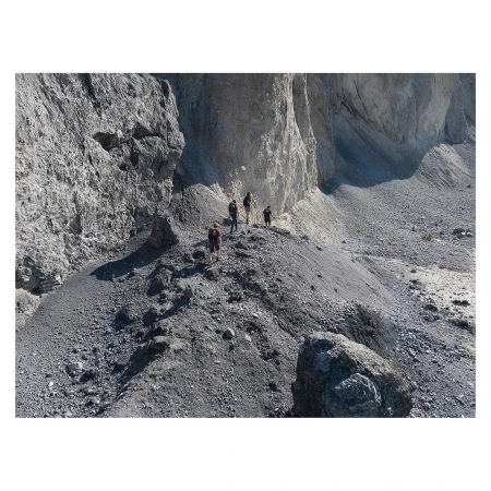 A group of hikers on a rocky mountain path. The path is narrow, and the hikers are surrounded by tall rock formations.
