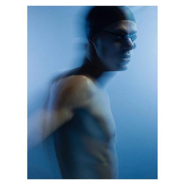 Motion blur portrait of swimmer with cap and goggles against blue background. Athletic and sporty, the swimmer looks onward in the blur.