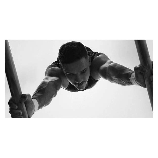 Monochrome shot of male gymnast performing on parallel bars, showing strength and focus in a clean, minimalist setting.
