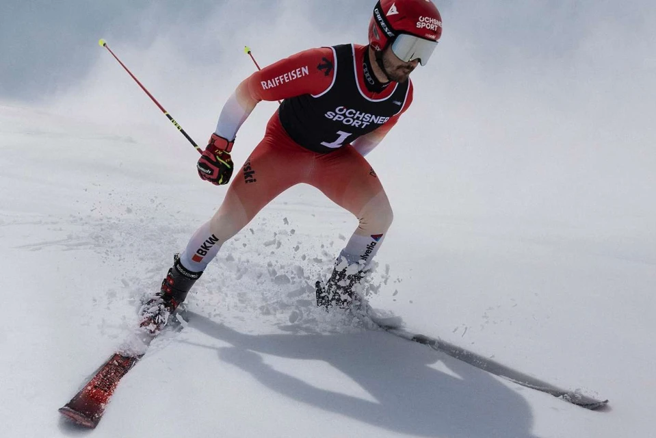 Downhill skier in red racing suit and gear speeding down snowy slope in a high-speed turn, captured at eye-level for dynamic action.