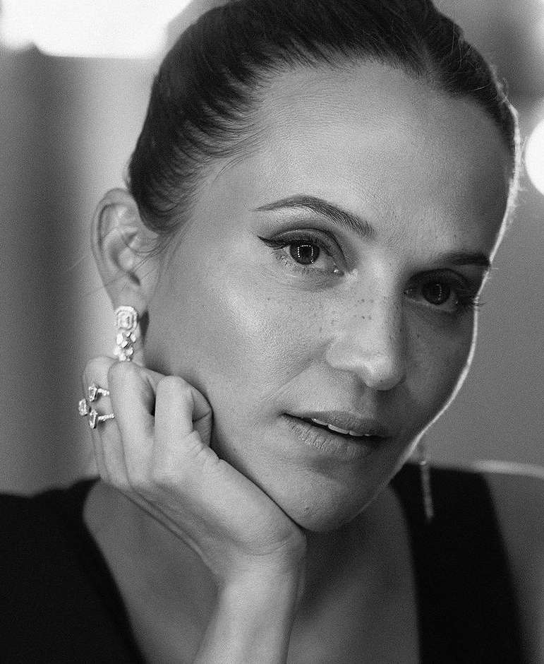 Close-up portrait of a woman resting her chin on her hand, wearing diamond rings and earrings, captured in monochrome by Sandro Baebler.