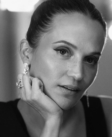 Close-up portrait of a woman resting her chin on her hand, wearing diamond rings and earrings, captured in monochrome by Sandro Baebler.