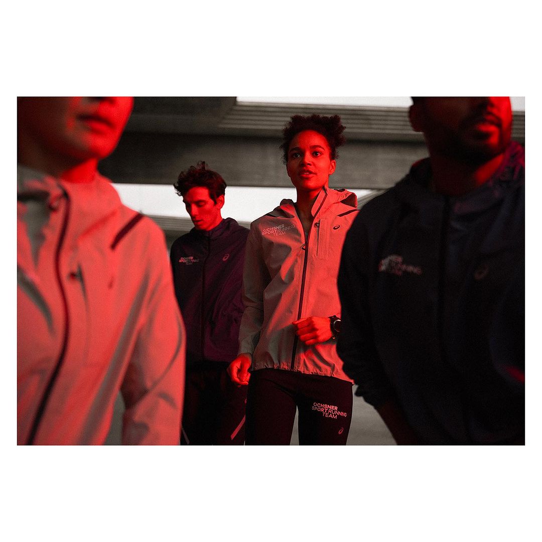 Group of runners wearing matching jackets in an urban setting with moody, low lighting and a shallow depth of field.