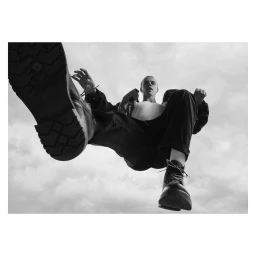 Low angle worm's-eye view of a man leaping in dark trousers and chunky boots against a cloudy sky