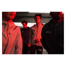 Four runners in athletic jackets standing outdoors under a concrete structure lit by red light