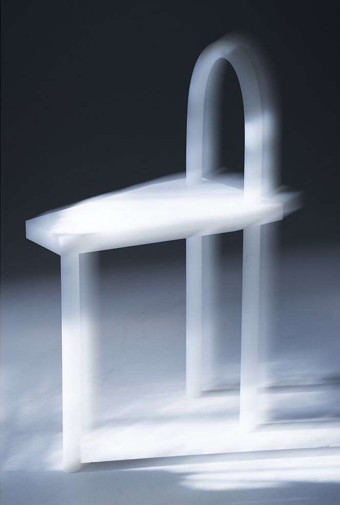 Minimalist white chair with arched back in soft, diffused lighting, showcasing modern furniture design and elegant simplicity on plain background.