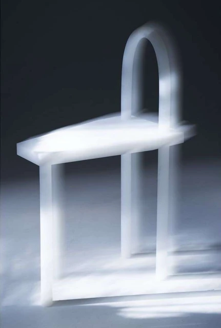Minimalist white chair with arched back in soft, diffused lighting, showcasing modern furniture design and elegant simplicity on plain background.