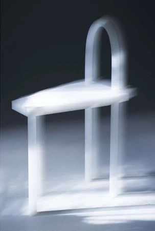 Minimalist white chair with arched back in soft, diffused lighting, showcasing modern furniture design and elegant simplicity on plain background.