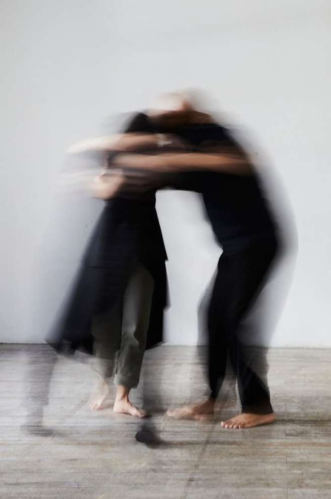 Motion blur image of two adults embracing in studio, capturing movement and connection with neutral backdrop and soft, diffused lighting.