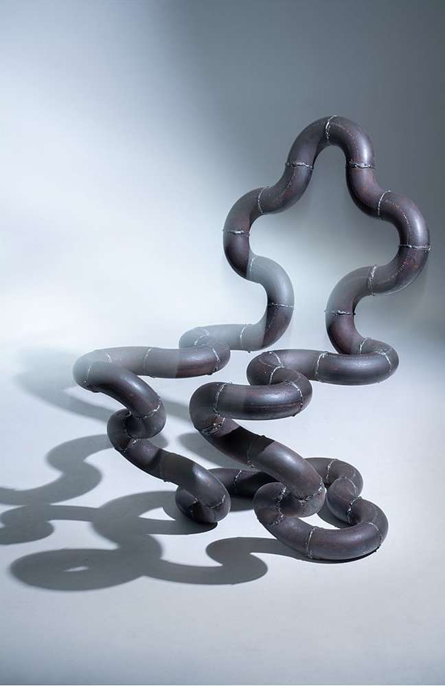 Abstract, brown looped tubing sculpture with geometric and organic forms set in a neutral studio environment with soft, diffused lighting.