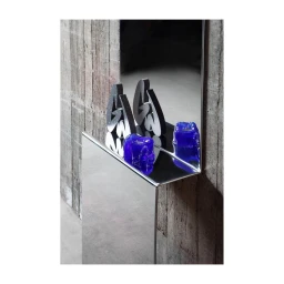 Reflective chrome console table displaying two blue glass objects and sculptural letters against concrete wall