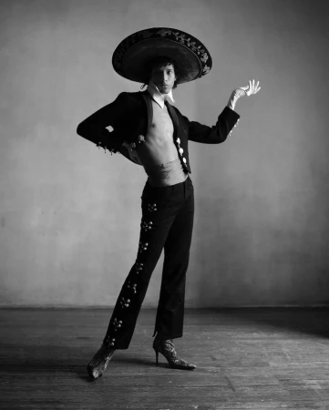 Monochrome portrait of a person wearing a mariachi sombrero, embroidered jacket, and heeled boots in a studio setting.