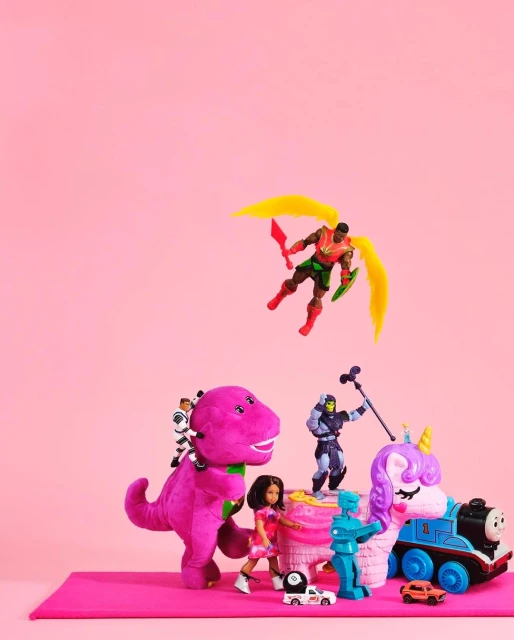 Toy figures and vehicles are displayed on a pink surface against a bright pink backdrop in a studio-style setup.