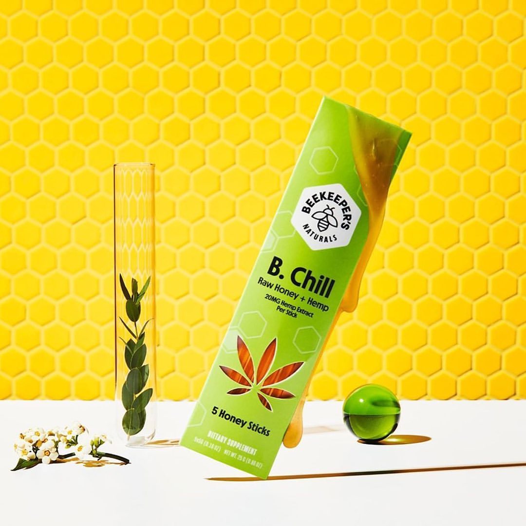 Beekeepers Naturals B. Chill honey sticks in lime-green packaging next to flower sprig, test tube with plant, and green sphere.