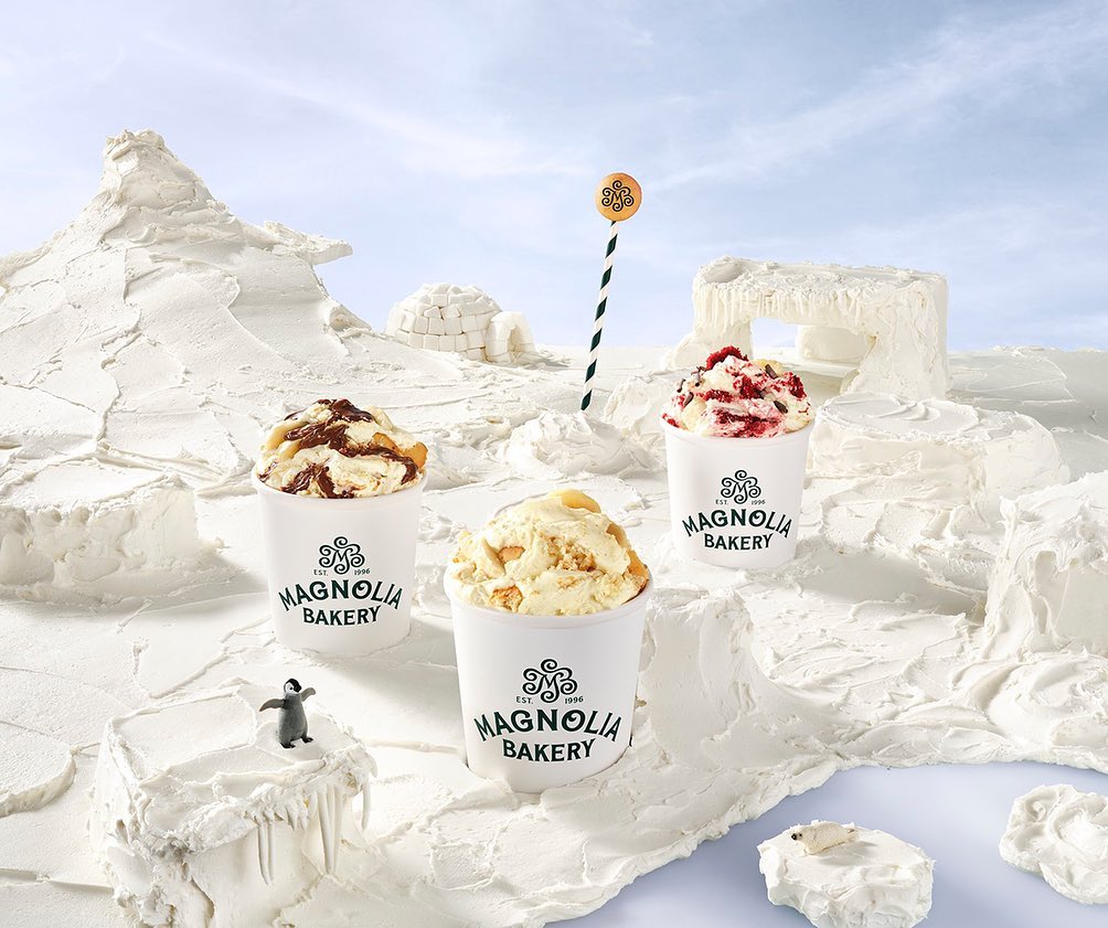 Three Magnolia Bakery ice cream cups sit on a white, snow-like landscape with a marker pole, an igloo, and a toy penguin and polar bear.