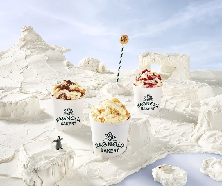 Three Magnolia Bakery ice cream cups sit on a white, snow-like landscape with a marker pole, an igloo, and a toy penguin and polar bear.