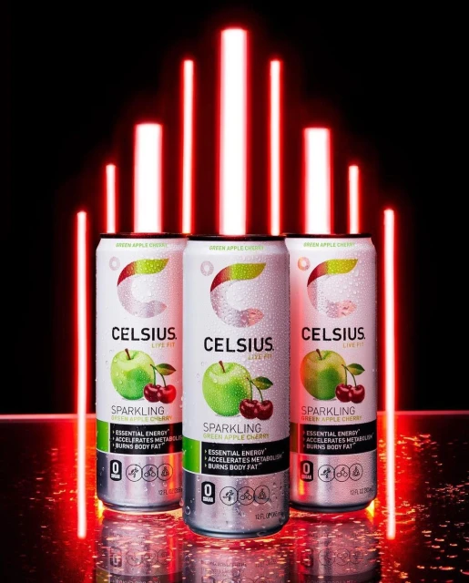 Three cans of Celsius brand sparkling green apple cherry energy drink with red LED bars in the background against a black backdrop.