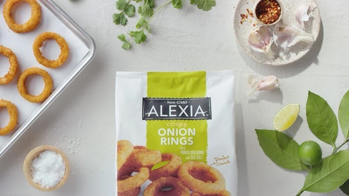 Overhead shot of frozen Alexia onion rings, alongside cilantro, limes, spices, and garlic on a white background, for a food and beverage theme.