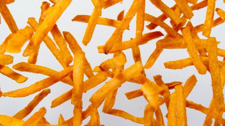 Overhead shot of golden-brown french-fried potatoes randomly scattered against a bright white background in a food and beverage setting.