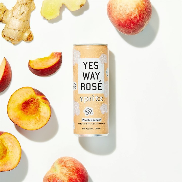 Elevated shot of Yes Way Rosé spritz can surrounded by fresh peaches and ginger against a white background, showcasing a beverage product.