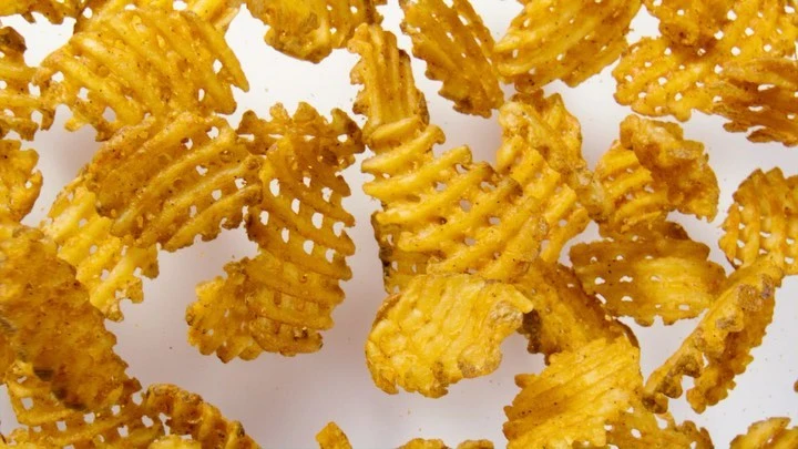 Close-up of golden brown waffle fries scattered on a white background, showcasing their textured surface and inviting appearance.