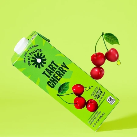 Elevated view of revitalizing tart cherry juice box, accompanied by vibrant cherries with droplet, against a light green backdrop.