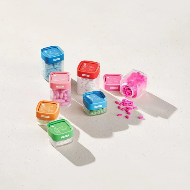 Colorful medicine capsules and pills displayed in translucent plastic containers with lids on a solid white surface and background.