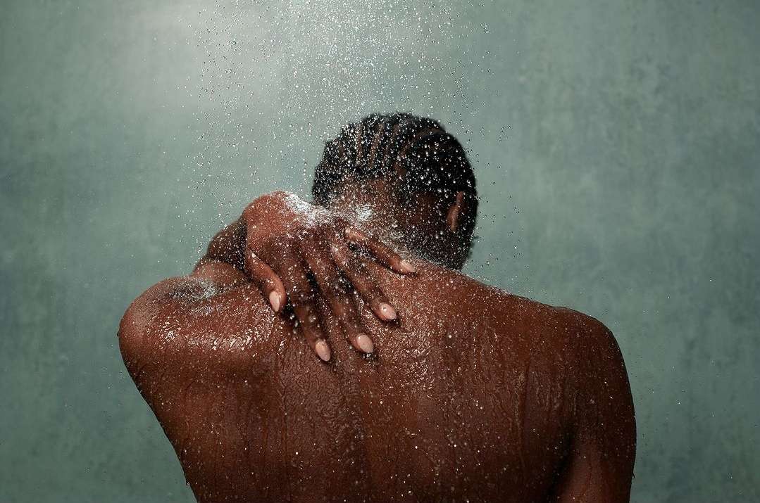 Close-up of an African American adult female in a shower. Water droplets cover her skin as she touches her upper back.