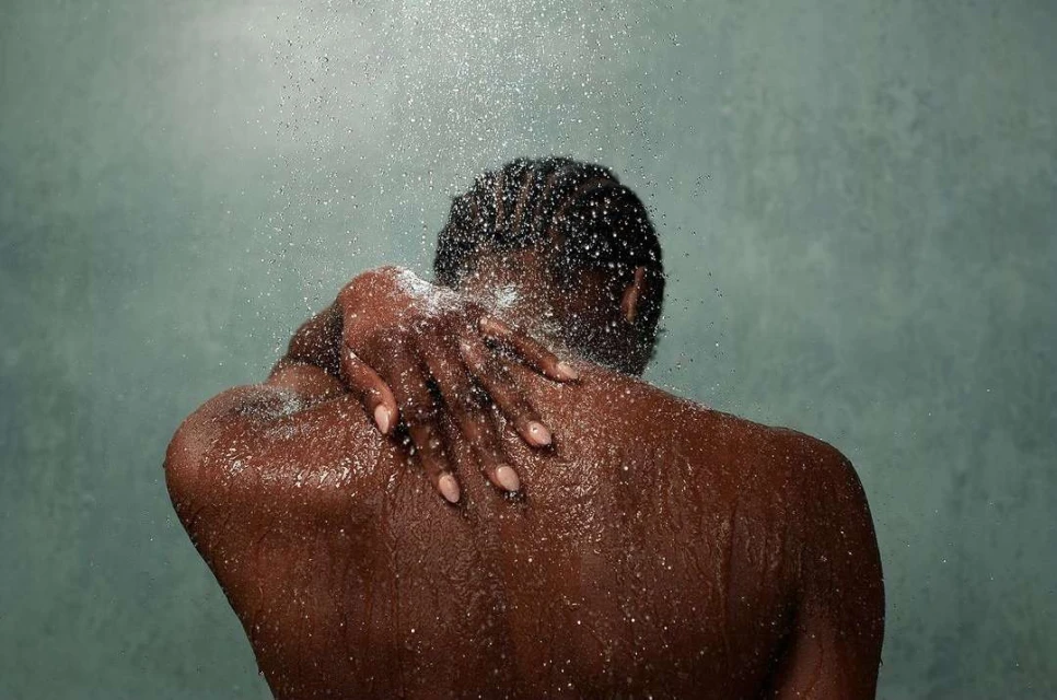Close-up of an African American adult female in a shower. Water droplets cover her skin as she touches her upper back.