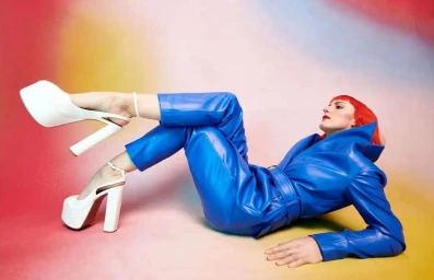 Woman in vibrant blue leather trousers and matching jacket wearing thick white platform heels lying down