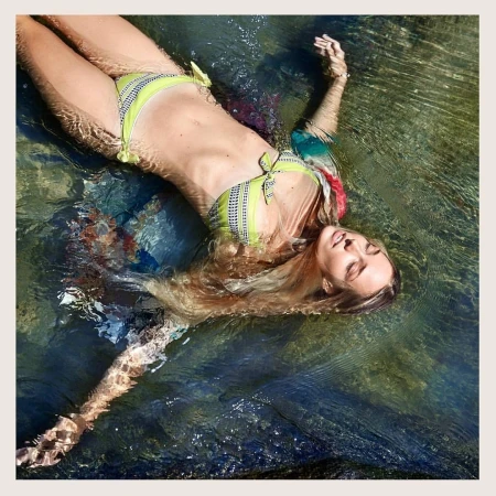 Woman in a yellow bikini floats on her back in clear water, surrounded by sunlight and ripples, creating a serene summertime image.