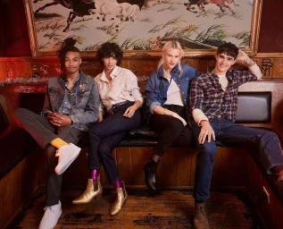 Group of four diverse models seated on a dark leather banquette booth beneath a framed painting of running horses.