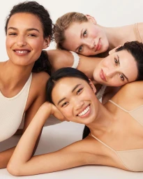 Four women smiling together with heads resting close in a circular studio portrait
