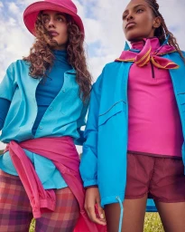 Two models outdoors against a cloudy sky wearing vibrant blue, pink, and red athletic apparel and bucket hats.