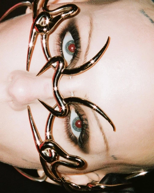 Portrait of a person wearing gold metallic jewelry around their eyes, capturing a close-up view of the jewelry and the person's facial features.