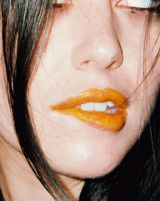 Close-up of a young woman's face showcasing gold lipstick and dark hair, emphasizing beauty and makeup in an indoor setting.