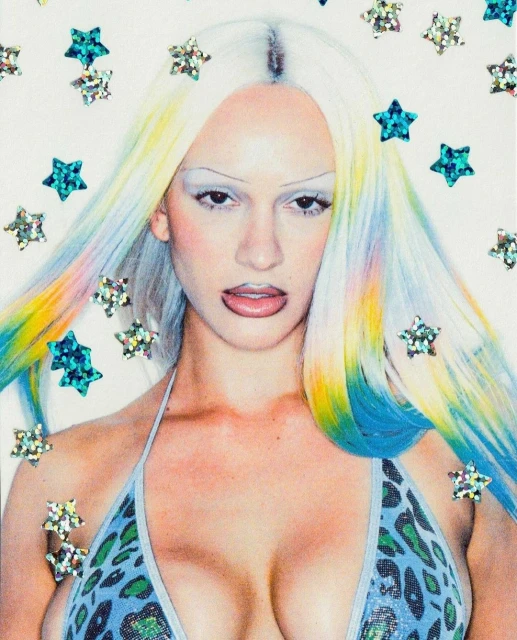 Close-up studio portrait of a woman with platinum and rainbow-colored hair, wearing a bikini top, against a white background with star decals.
