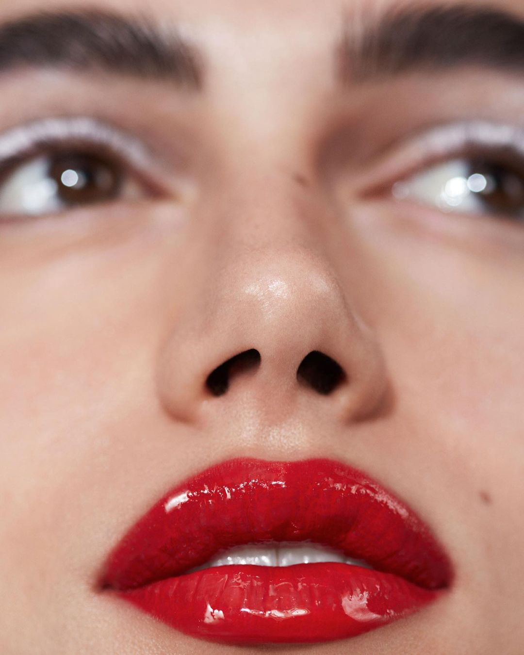Close-up of an adult female face with glossy red lipstick and white eyeliner in a beauty shot, focusing on eyes, nose, and lips.