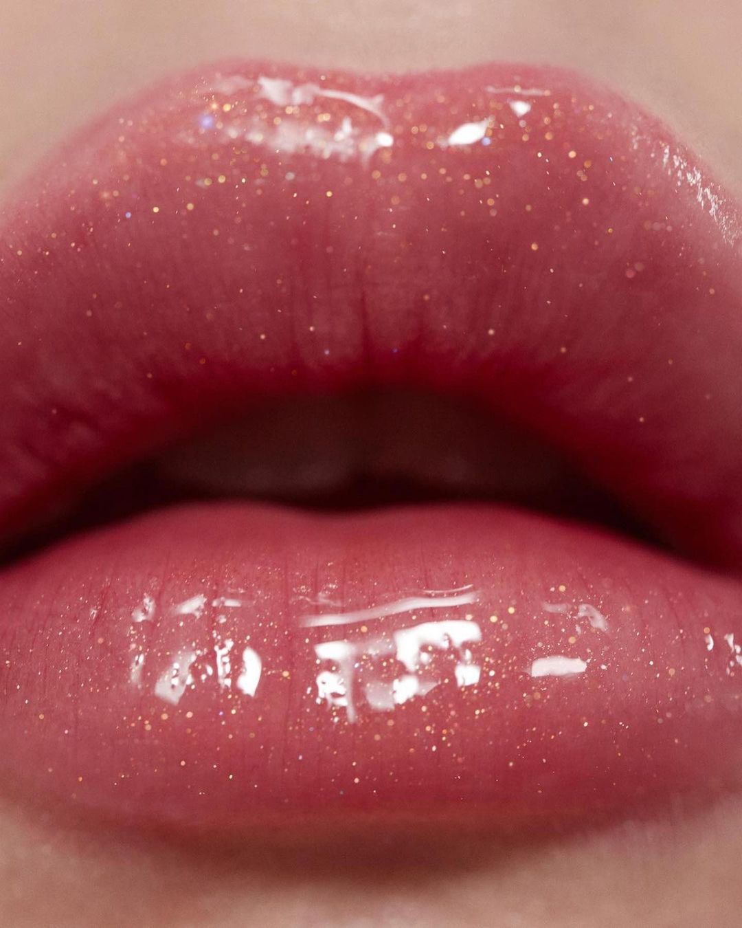 Macro photograph of an adult female's glossy lips coated in shimmering, light pink lip gloss that reflects the light.